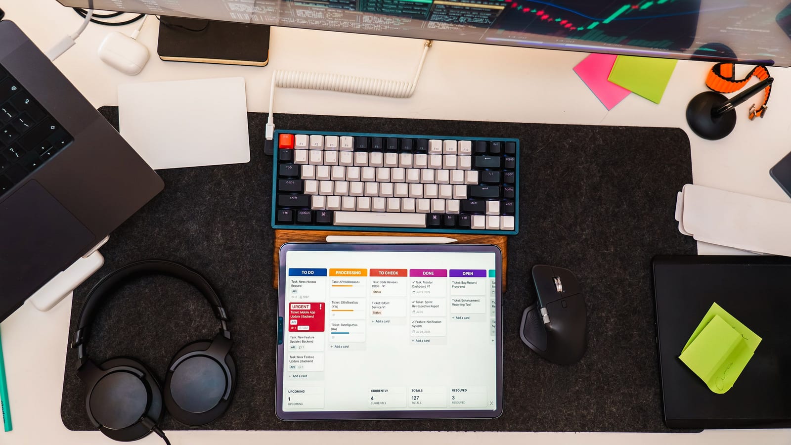 Top view of a tech workspace featuring a digital tablet, keyboard, monitor, and headphones for project management.