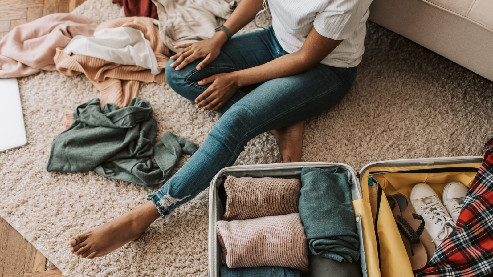 Woman organizing clothes while sitting on floor with open suitcase, preparing for a trip.