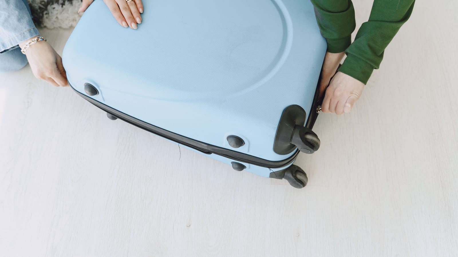 Unrecognizable female friends in casual clothes sitting on floor with fluffy carpet and opening suitcase together while preparing for journey and adventure