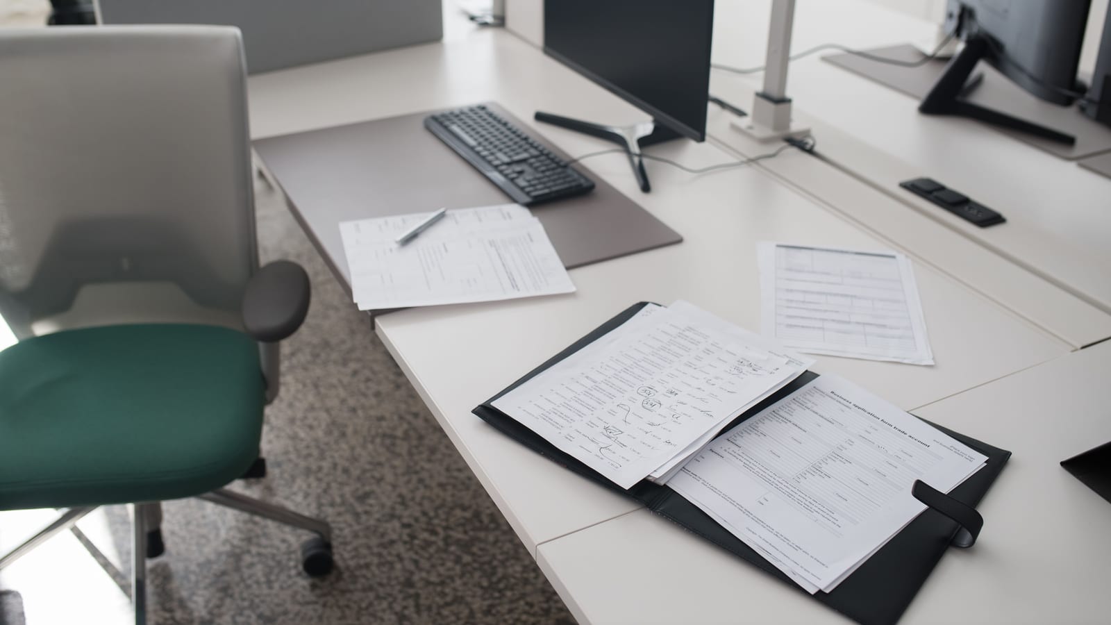 A clean and organized office desk with documents, a computer, and chair in a modern workspace.