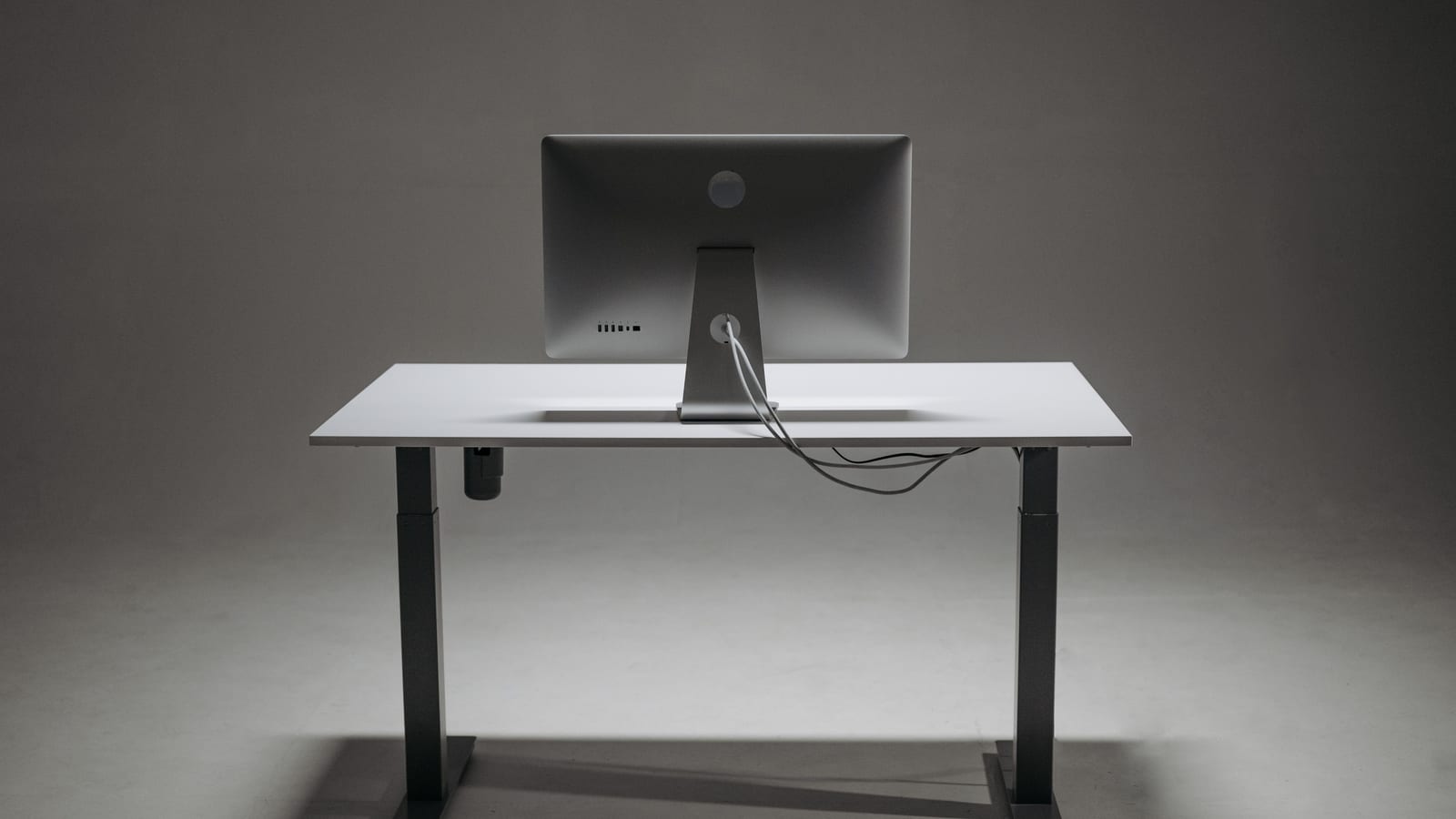 Rear view of a modern height adjustable standing desk with monitor and cable management.