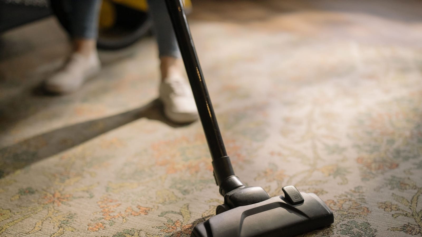 Close-up of a vacuum cleaner on a patterned carpet in a sunlit room, capturing a moment of household cleaning.