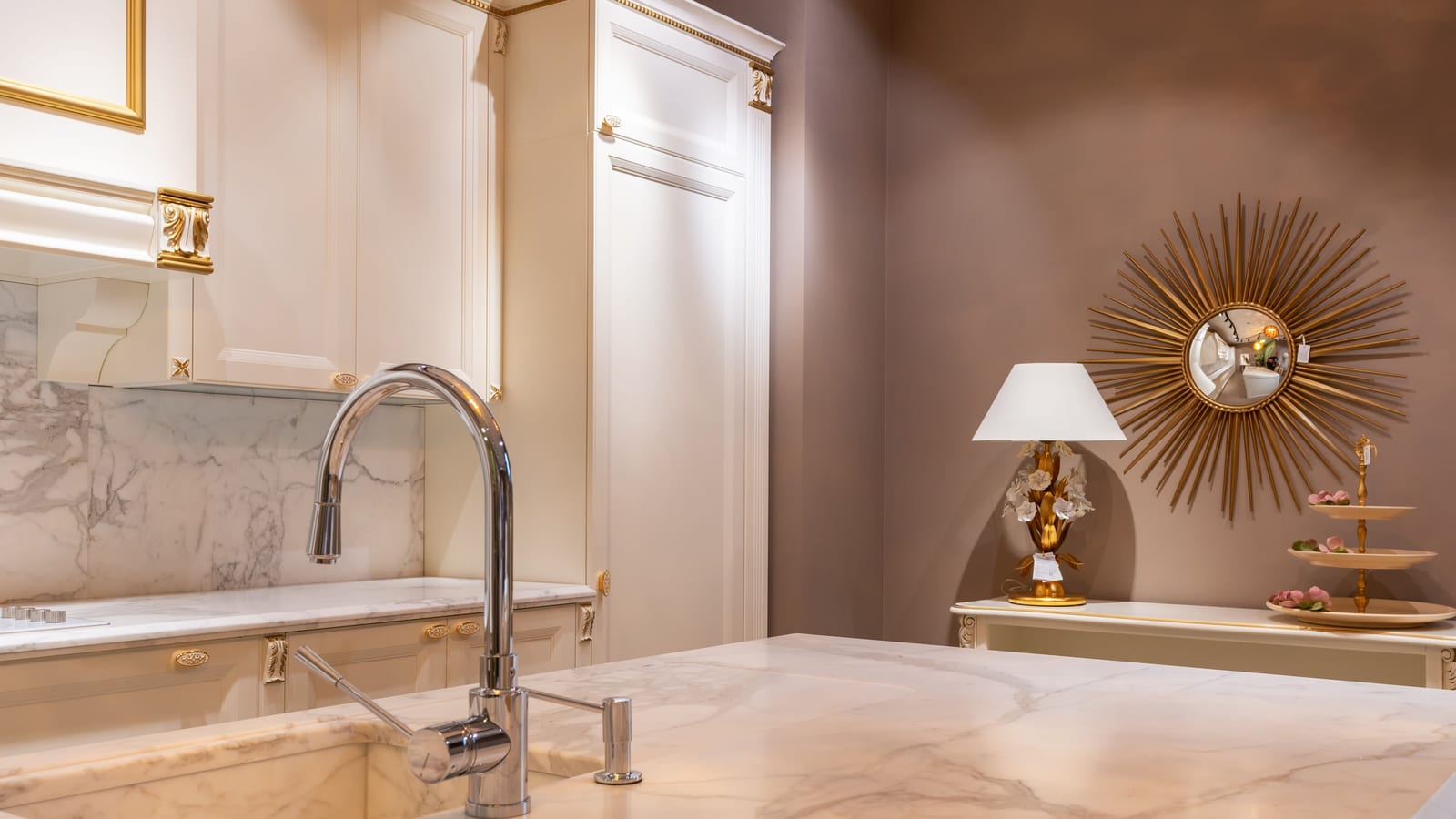 Sink with faucet on marble counter in modern stylish kitchen with white cabinets and glowing lamp near decorations in apartment